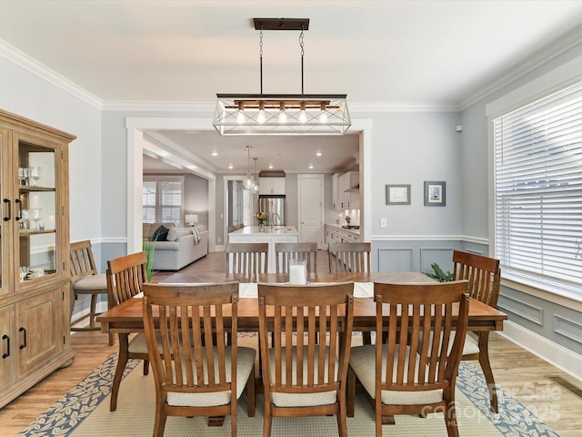 dining room featuring a wainscoted wall, crown molding, a decorative wall, and light wood finished floors