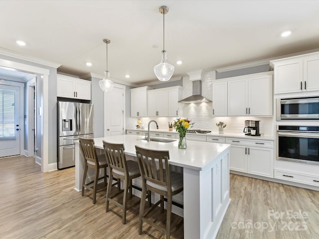 kitchen featuring ornamental molding, stainless steel appliances, light countertops, wall chimney range hood, and a sink