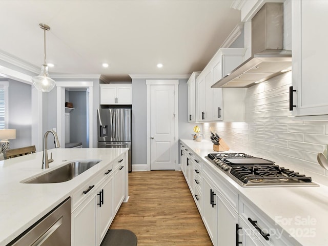 kitchen featuring white cabinets, appliances with stainless steel finishes, light countertops, wall chimney range hood, and a sink