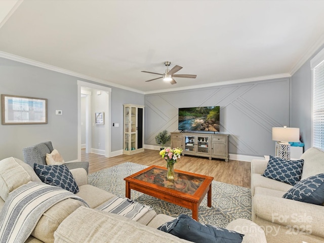 living room featuring light wood finished floors, ceiling fan, ornamental molding, and baseboards