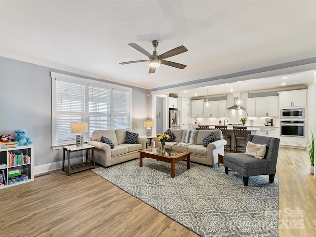 living room featuring ceiling fan, ornamental molding, light wood-type flooring, and baseboards