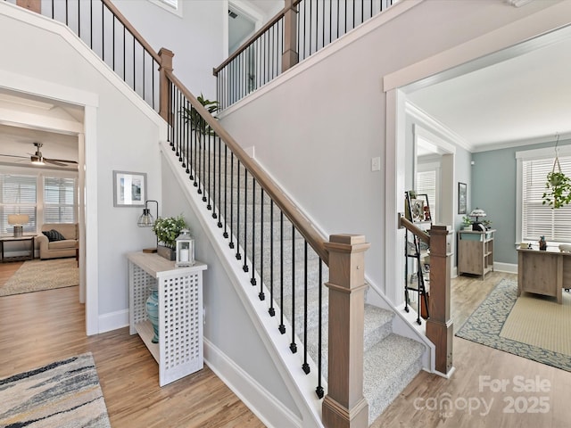 staircase featuring baseboards, a ceiling fan, a towering ceiling, ornamental molding, and wood finished floors