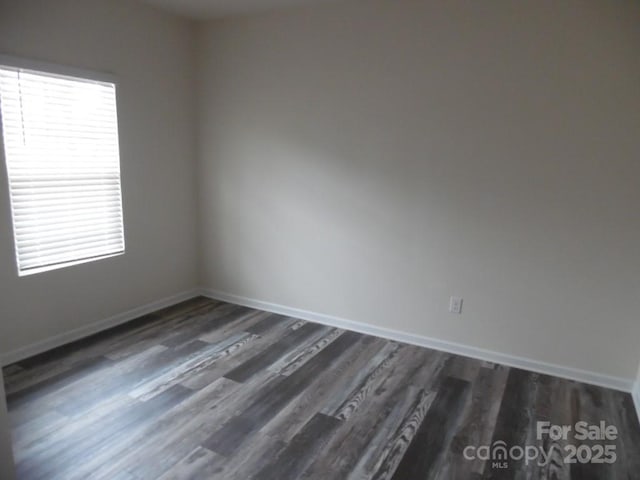 empty room featuring dark wood-type flooring, a wealth of natural light, and baseboards