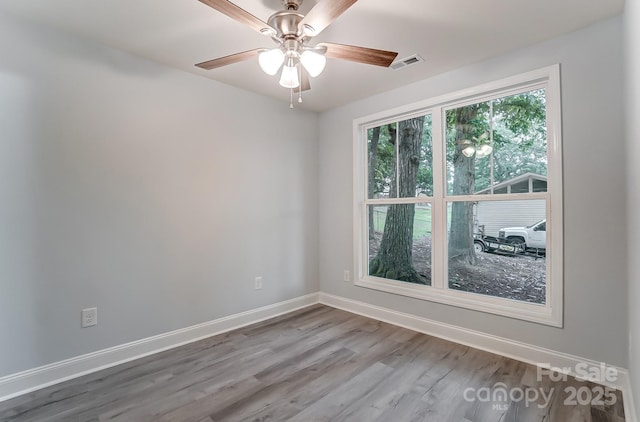 empty room with a ceiling fan, wood finished floors, visible vents, and baseboards