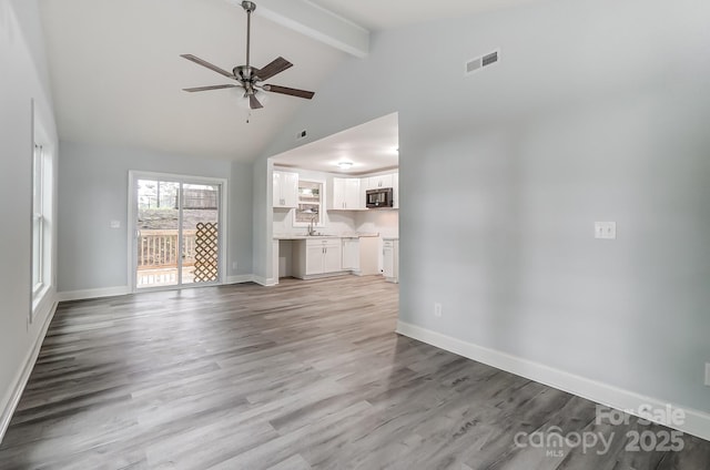 unfurnished living room featuring visible vents, beamed ceiling, light wood-style flooring, and baseboards