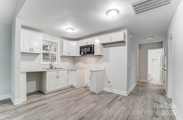 kitchen with black microwave, a sink, visible vents, and white cabinetry