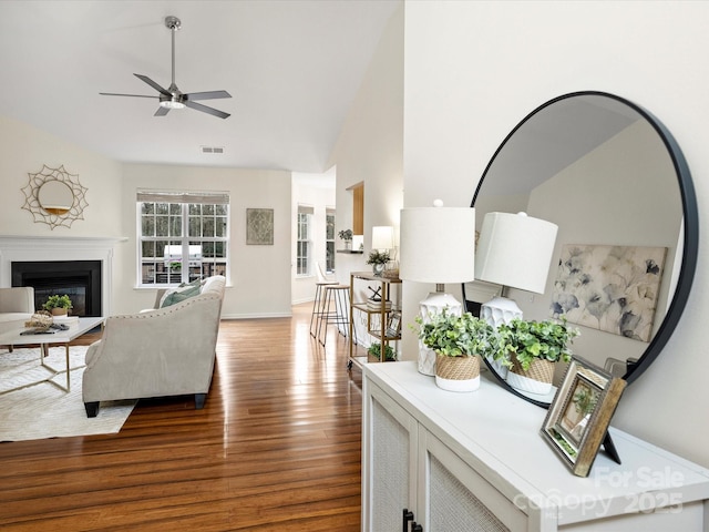 living room featuring a ceiling fan, wood finished floors, visible vents, lofted ceiling, and a fireplace