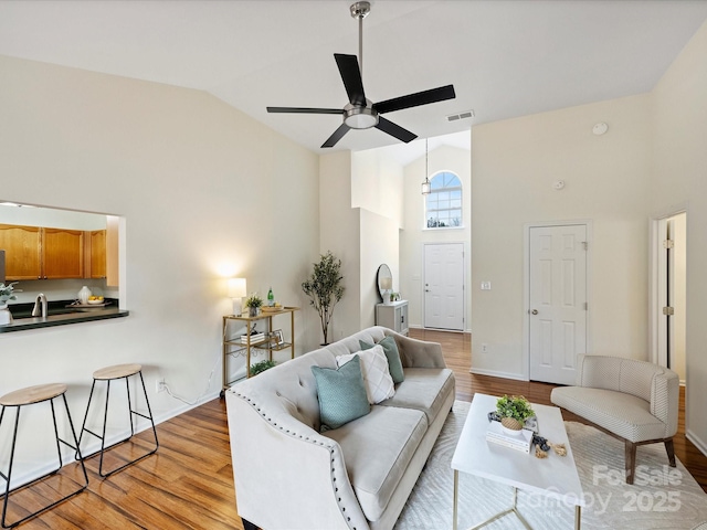 living room featuring a ceiling fan, baseboards, visible vents, high vaulted ceiling, and light wood-style flooring