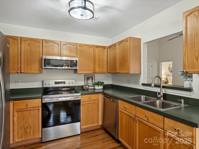 kitchen with a sink, stainless steel appliances, dark countertops, and dark wood finished floors