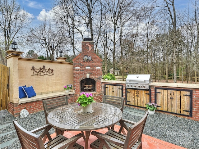 view of patio featuring fence, exterior kitchen, area for grilling, outdoor dining area, and an outdoor brick fireplace