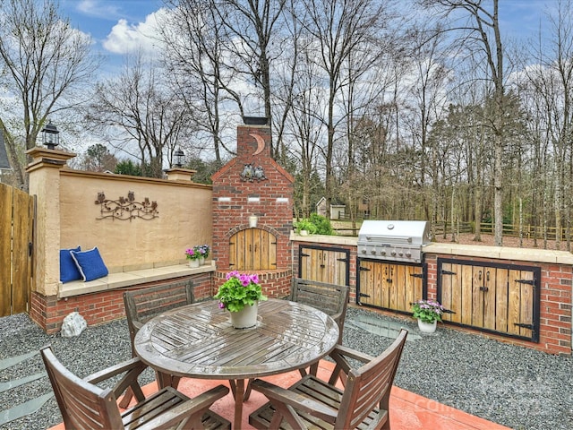 wooden terrace with an outdoor brick fireplace, fence, an outdoor kitchen, a grill, and a patio