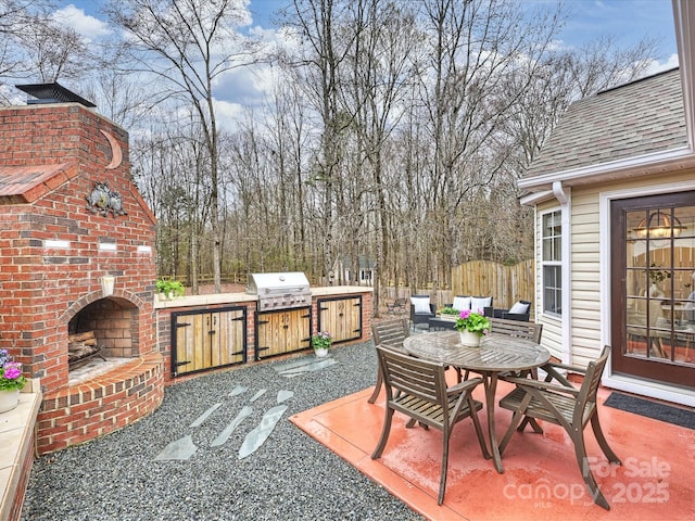 view of patio / terrace featuring fence, exterior kitchen, outdoor dining area, an outdoor brick fireplace, and grilling area