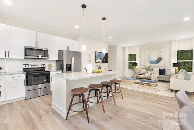 kitchen with decorative light fixtures, appliances with stainless steel finishes, open floor plan, white cabinets, and a kitchen island