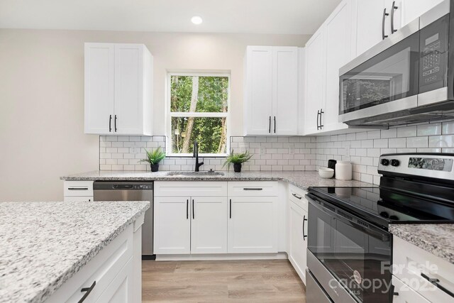 kitchen with white cabinets, light wood-style flooring, light stone counters, appliances with stainless steel finishes, and a sink