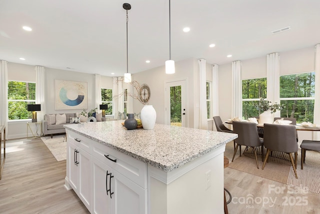 kitchen with visible vents, white cabinets, light stone counters, hanging light fixtures, and light wood-style floors