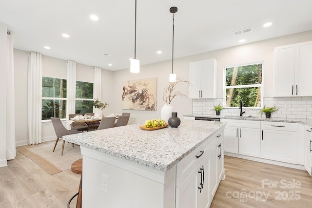 kitchen with hanging light fixtures, white cabinetry, a kitchen island, and visible vents