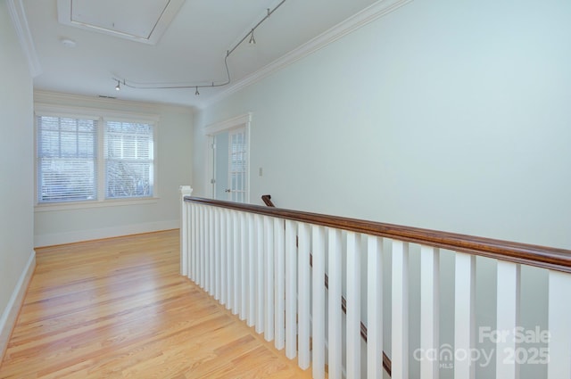 corridor featuring baseboards, ornamental molding, light wood-type flooring, attic access, and rail lighting