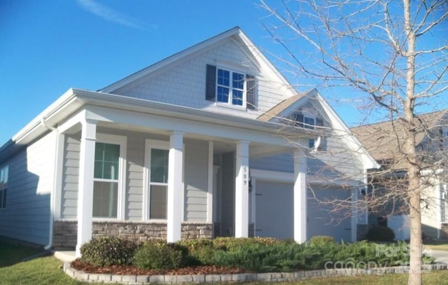 view of front of home featuring a garage, stone siding, and a porch