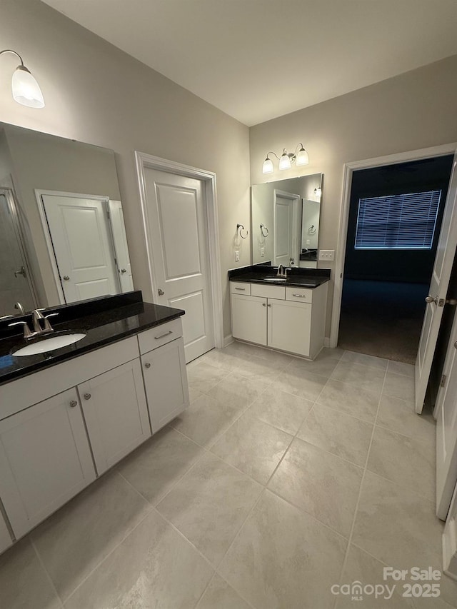 bathroom featuring baseboards, two vanities, a sink, and tile patterned floors