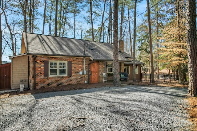 view of front of property with a shingled roof, a chimney, fence, and brick siding