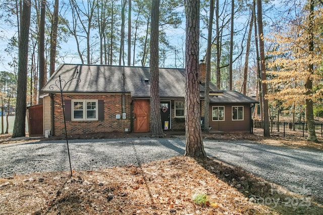 view of front facade featuring a shingled roof, a chimney, fence, and brick siding