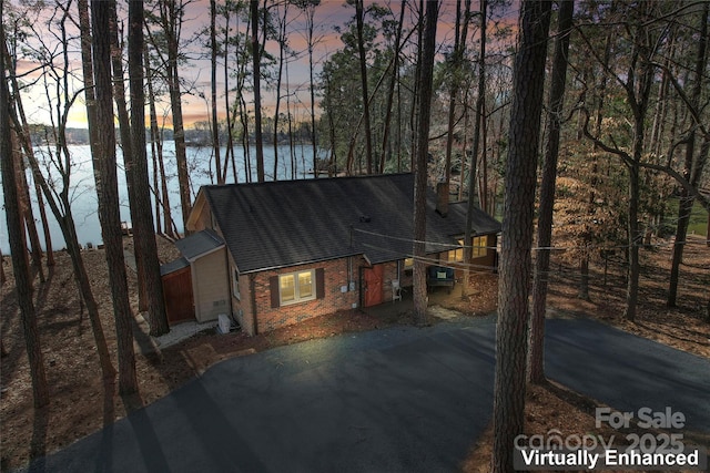 rustic home with aphalt driveway, brick siding, a water view, and a shingled roof