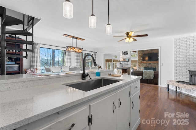 kitchen featuring ceiling fan, a fireplace, a sink, dark wood finished floors, and pendant lighting