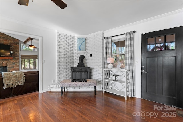 entrance foyer with lofted ceiling, a ceiling fan, ornamental molding, a wood stove, and wood finished floors