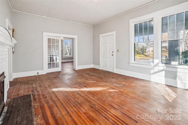 unfurnished living room featuring a brick fireplace, baseboards, a wealth of natural light, and wood finished floors