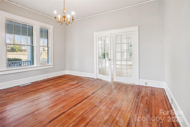 unfurnished room with wood finished floors, visible vents, baseboards, and an inviting chandelier