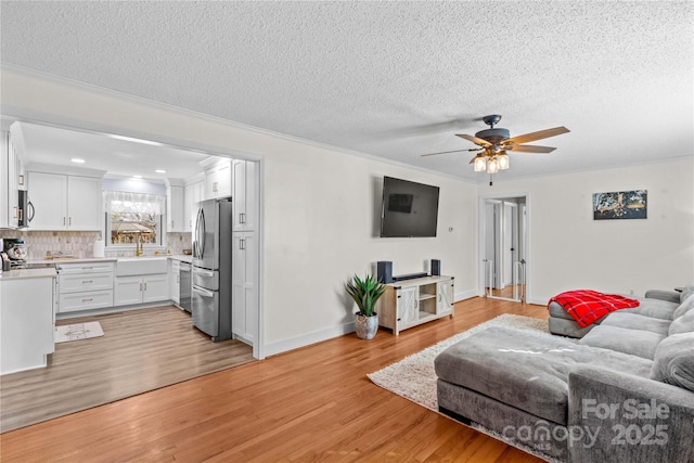 living area with ceiling fan, a textured ceiling, baseboards, and light wood-style floors