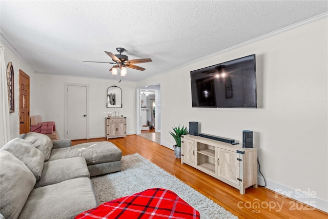 living area with baseboards, ceiling fan, wood finished floors, crown molding, and a textured ceiling