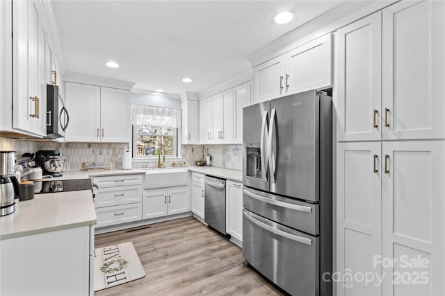 kitchen with appliances with stainless steel finishes, backsplash, light wood-type flooring, white cabinetry, and a sink