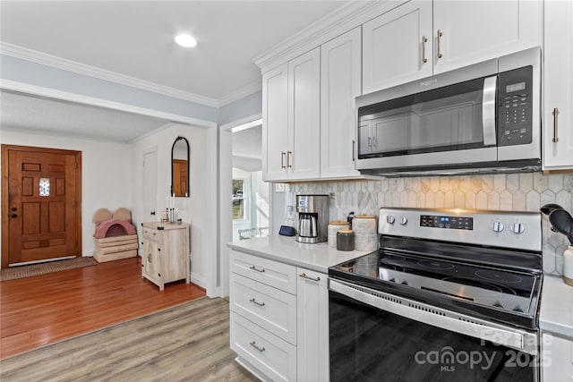 kitchen with stainless steel appliances, light countertops, light wood-style flooring, ornamental molding, and white cabinetry