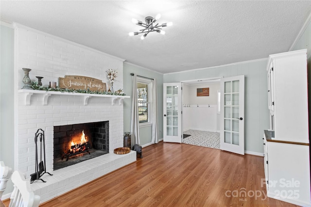 unfurnished living room with a notable chandelier, ornamental molding, a brick fireplace, a textured ceiling, and wood finished floors