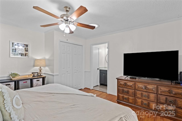 bedroom featuring a textured ceiling, connected bathroom, a ceiling fan, light wood-style floors, and a closet