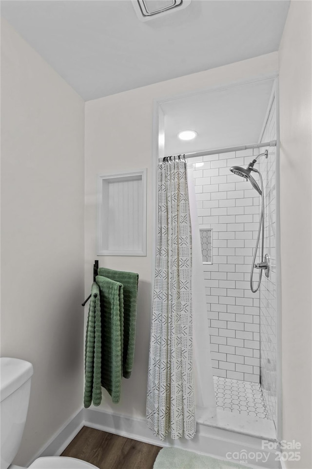 full bath featuring wood finished floors, a shower stall, toilet, and baseboards