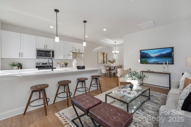 living area featuring light wood-type flooring, visible vents, an inviting chandelier, and recessed lighting