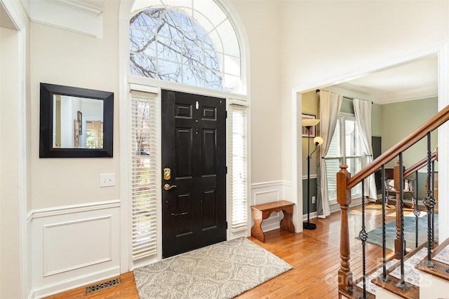 foyer entrance with hardwood / wood-style flooring, a high ceiling, visible vents, and wainscoting