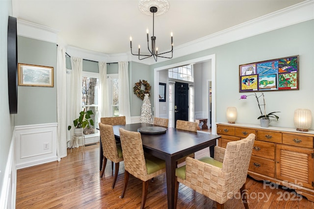 dining room featuring light wood finished floors, a decorative wall, ornamental molding, wainscoting, and a chandelier