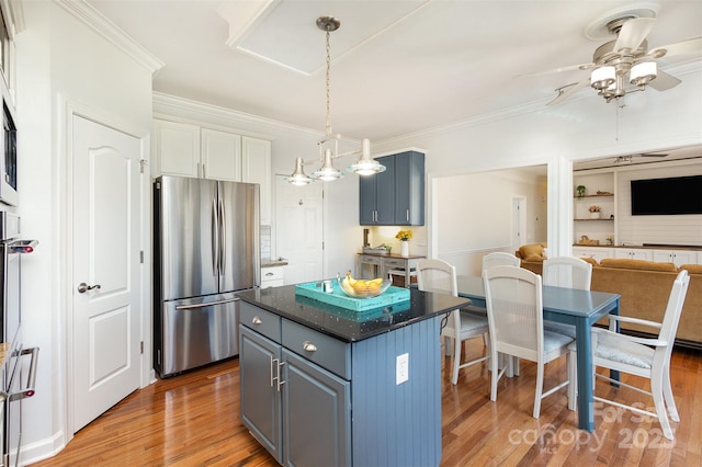 kitchen with wood finished floors, a kitchen island, a ceiling fan, ornamental molding, and freestanding refrigerator