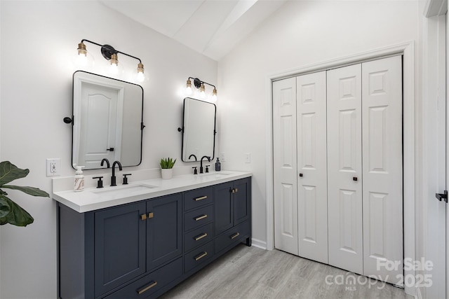 full bath with vaulted ceiling, double vanity, wood finished floors, and a sink