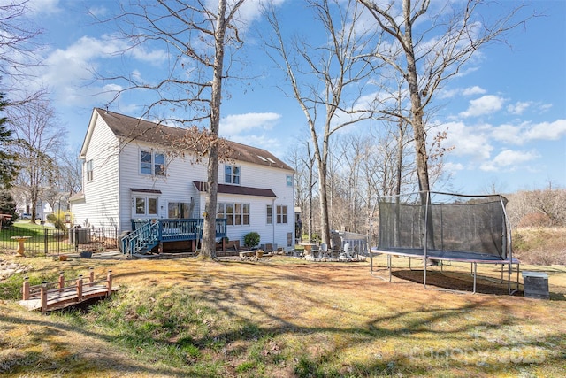 rear view of property with a trampoline, a yard, a deck, and fence