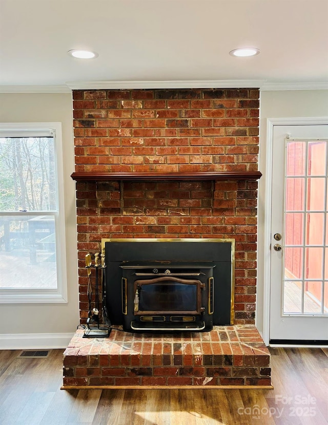 interior details featuring a wood stove, crown molding, baseboards, and wood finished floors