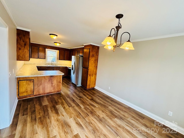 kitchen with decorative light fixtures, light countertops, a sink, stainless steel fridge, and a peninsula