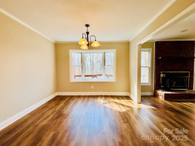 unfurnished dining area with baseboards, ornamental molding, wood finished floors, a fireplace, and a chandelier