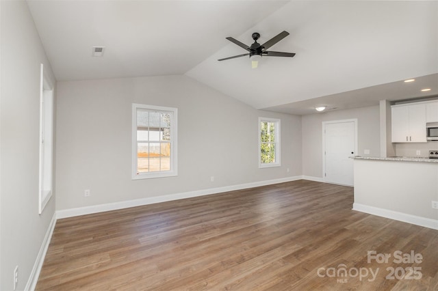 unfurnished living room with lofted ceiling, ceiling fan, light wood-style flooring, visible vents, and baseboards