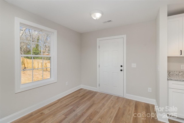 unfurnished room with light wood finished floors, visible vents, and baseboards