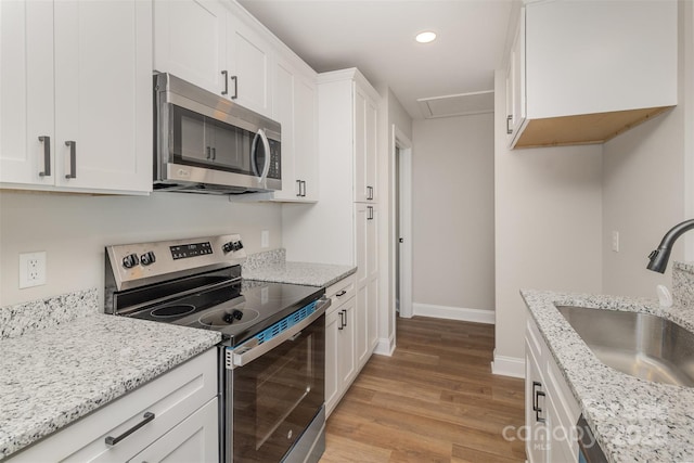 kitchen featuring light stone counters, light wood finished floors, stainless steel appliances, white cabinets, and a sink