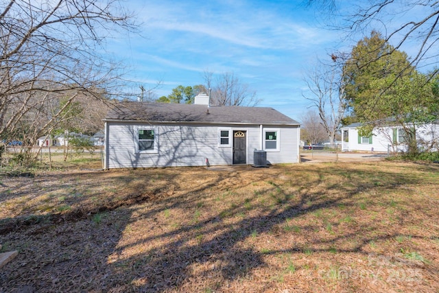 rear view of house with central AC unit, a lawn, a chimney, and fence